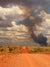 Red dirt road leading into the Australian outback with smoke rising in the distance under a dramatic cloudy sky, illustrating GPS tracking for remote area monitoring.