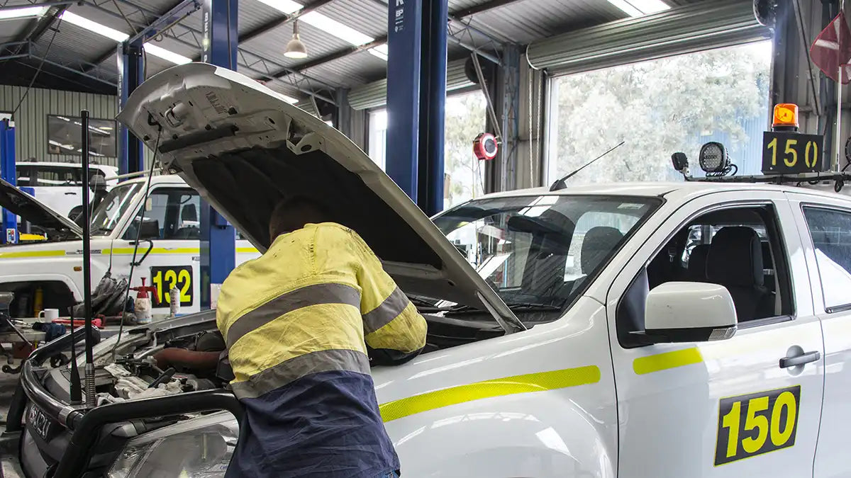 Mechanic working on a fleet vehicle in a workshop, representing installation and maintenance of hardwired GPS tracking systems for commercial fleets in Australia.