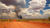 Remote Australian dirt track with distant smoke plume under stormy clouds, showing the value of GPS tracking for isolated locations.