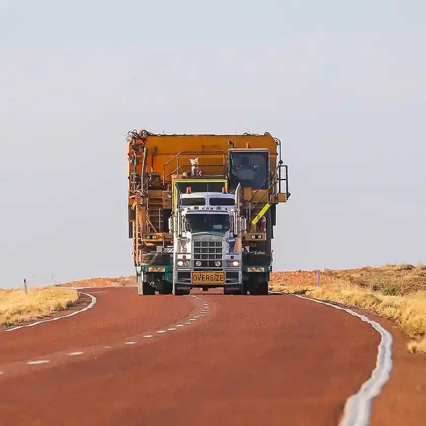 Large oversize truck transporting mining equipment on an outback highway, representing fleet tracking and GPS management for heavy haulage in Australia.
